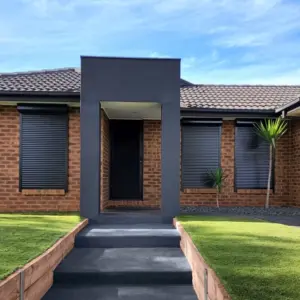 Front view of a brick home with modern roller shutter windows installed on either side of the entryway