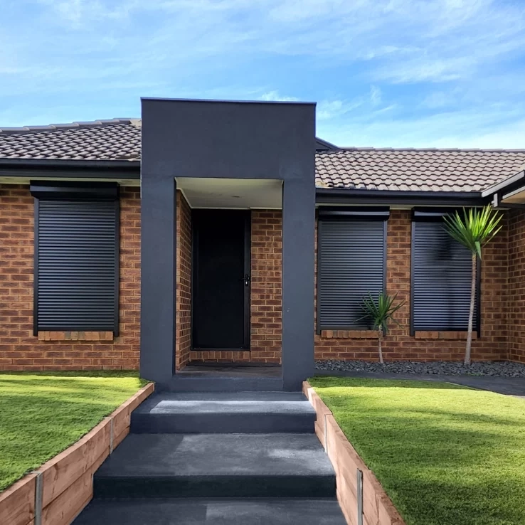 Front view of a brick home with modern roller shutter windows installed on either side of the entryway